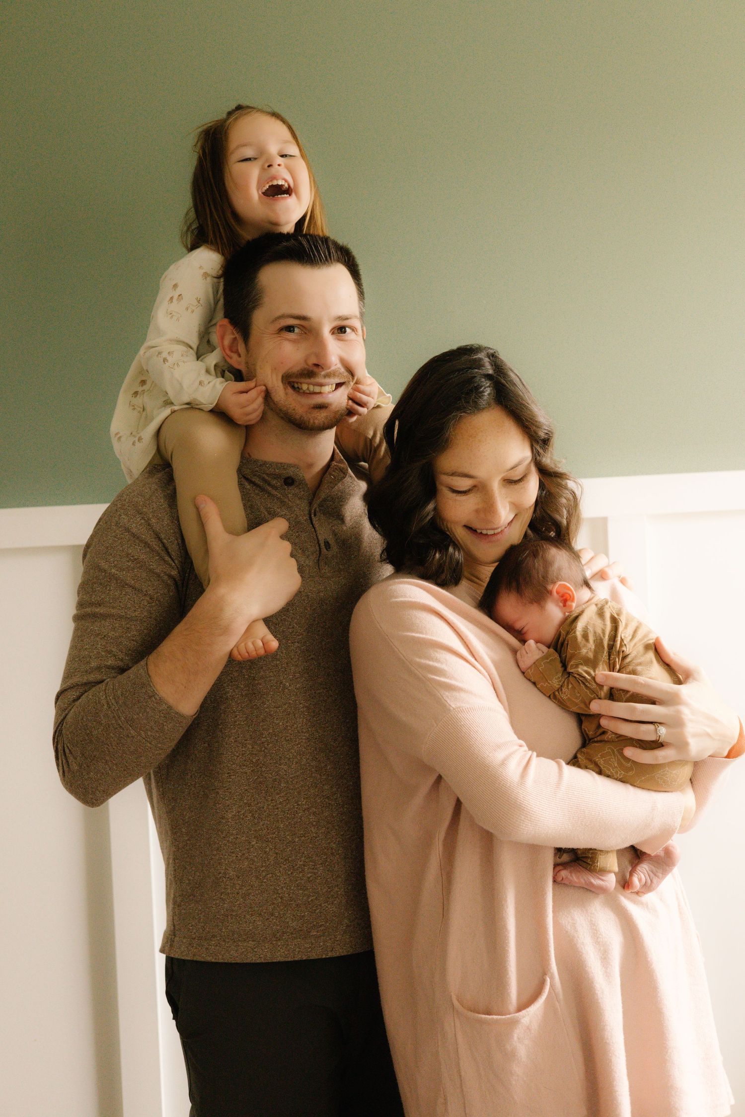 A joyful family portrait showing parents with their children in warm neutral tones against a simple wall background.