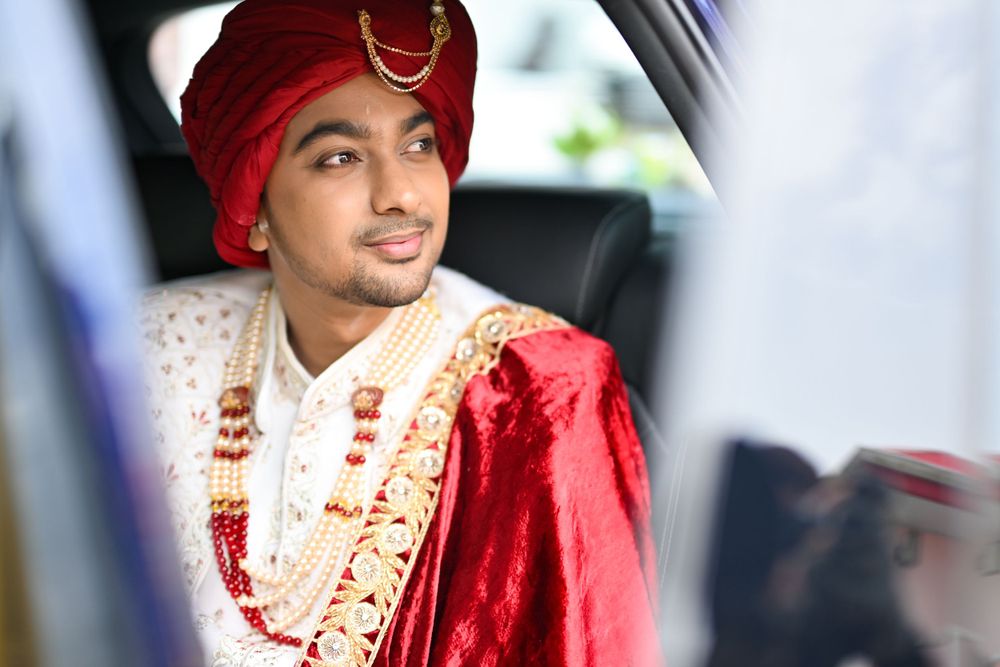 Groom in traditional Indian attire and red turban seated in car.