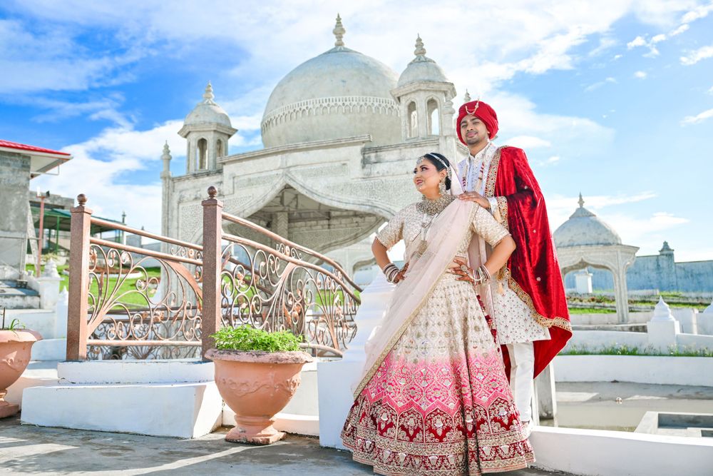 Indian wedding couple in traditional attire pose at white domed architectural setting.