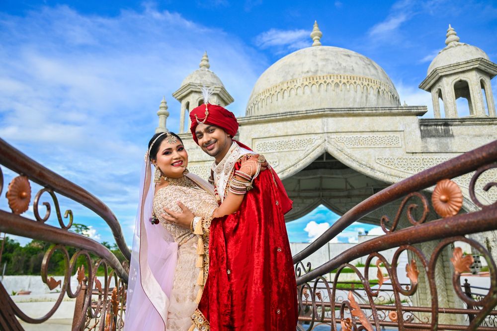 Indian wedding couple embracing in front of ornate white domed architecture.