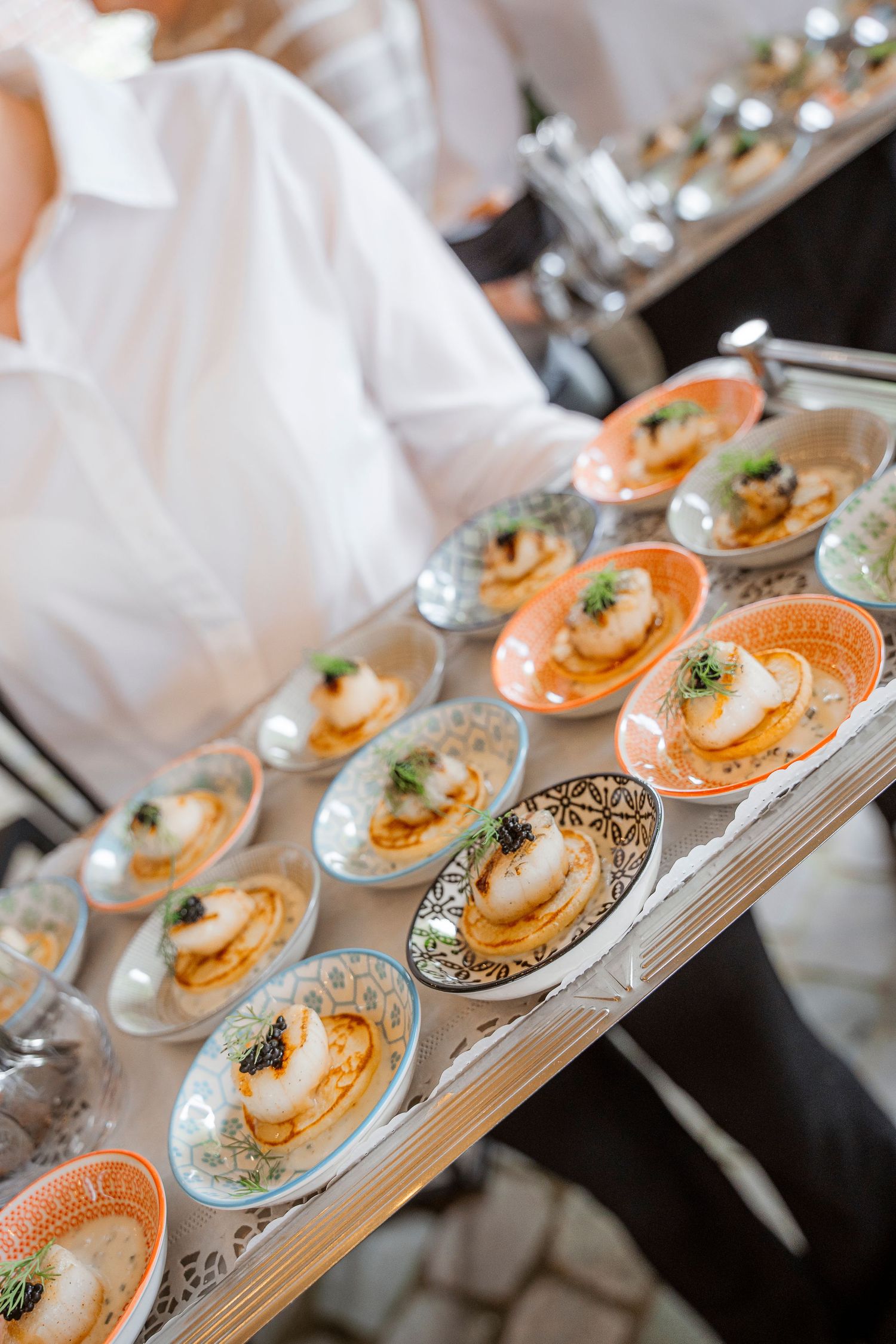 Elegantly plated appetizers on small dishes being served on silver tray at formal event.