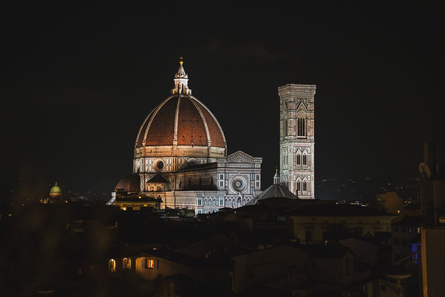 Florence Cathedral dome and bell tower illuminated at night against dark sky.