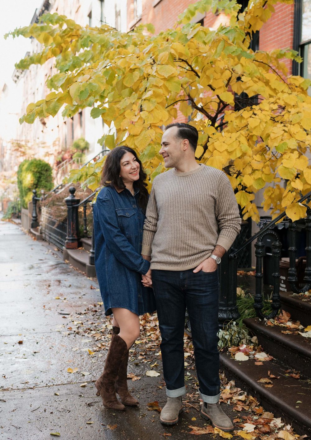 A couple enjoys a romantic autumn stroll on a brick-lined street with golden leaves falling from trees above.