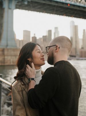 Romantic couple sharing intimate moments by the waterfront with the Brooklyn city skyline at sunset.