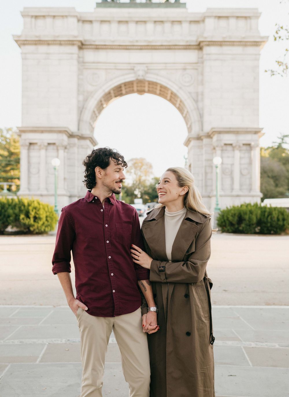 A happy couple shares a joyful moment together in front of a grand stone archway on a sunny day.
