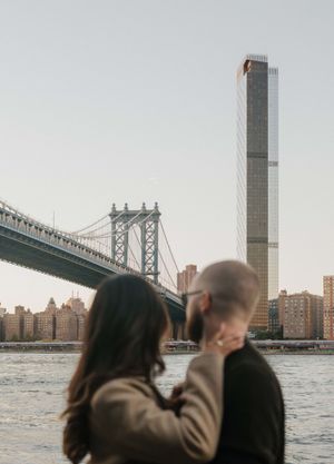 Couple embracing with Manhattan Bridge and NYC skyline in the background at golden hour.