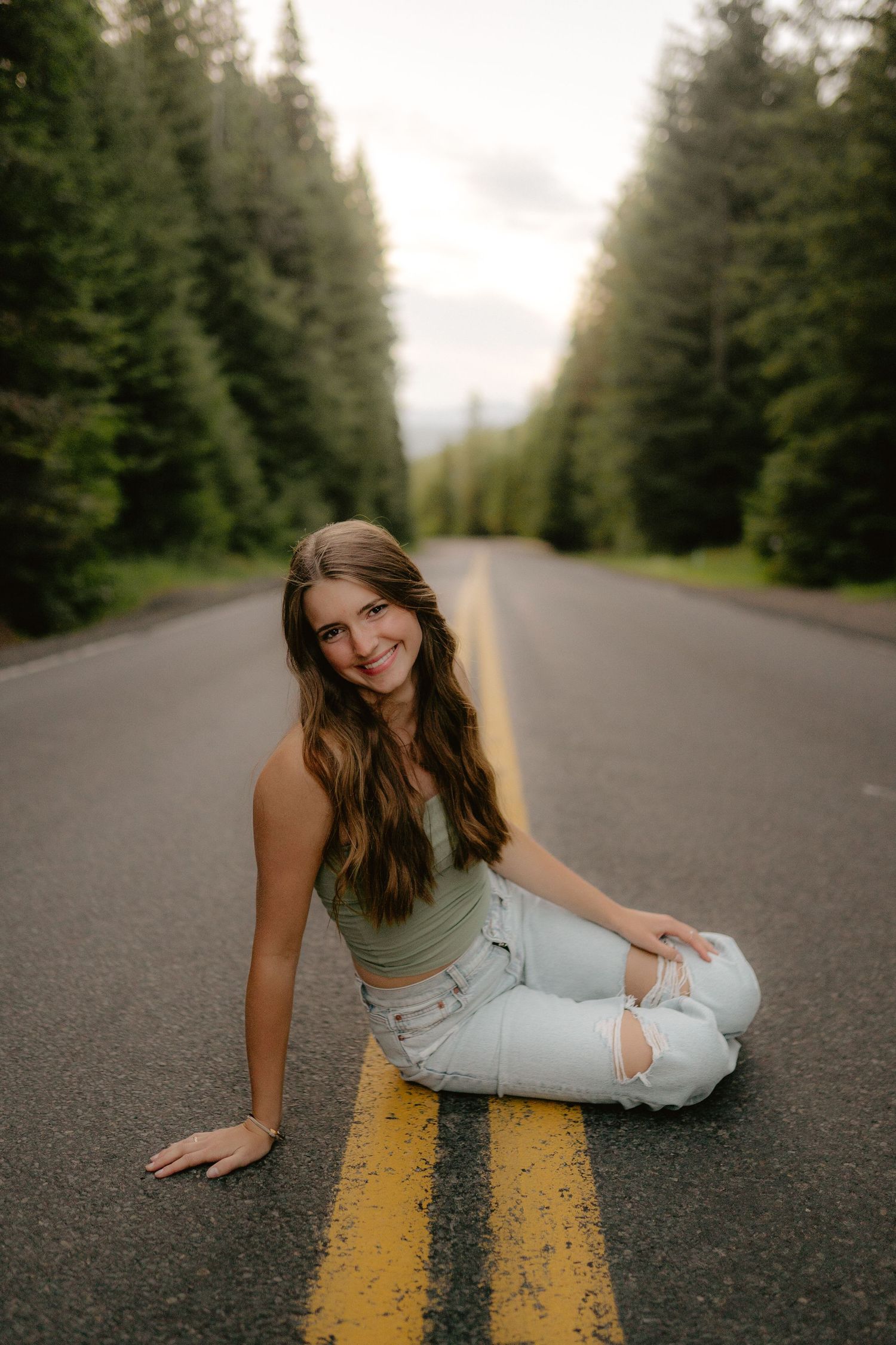 Person lounging on yellow road lines through evergreen forest.