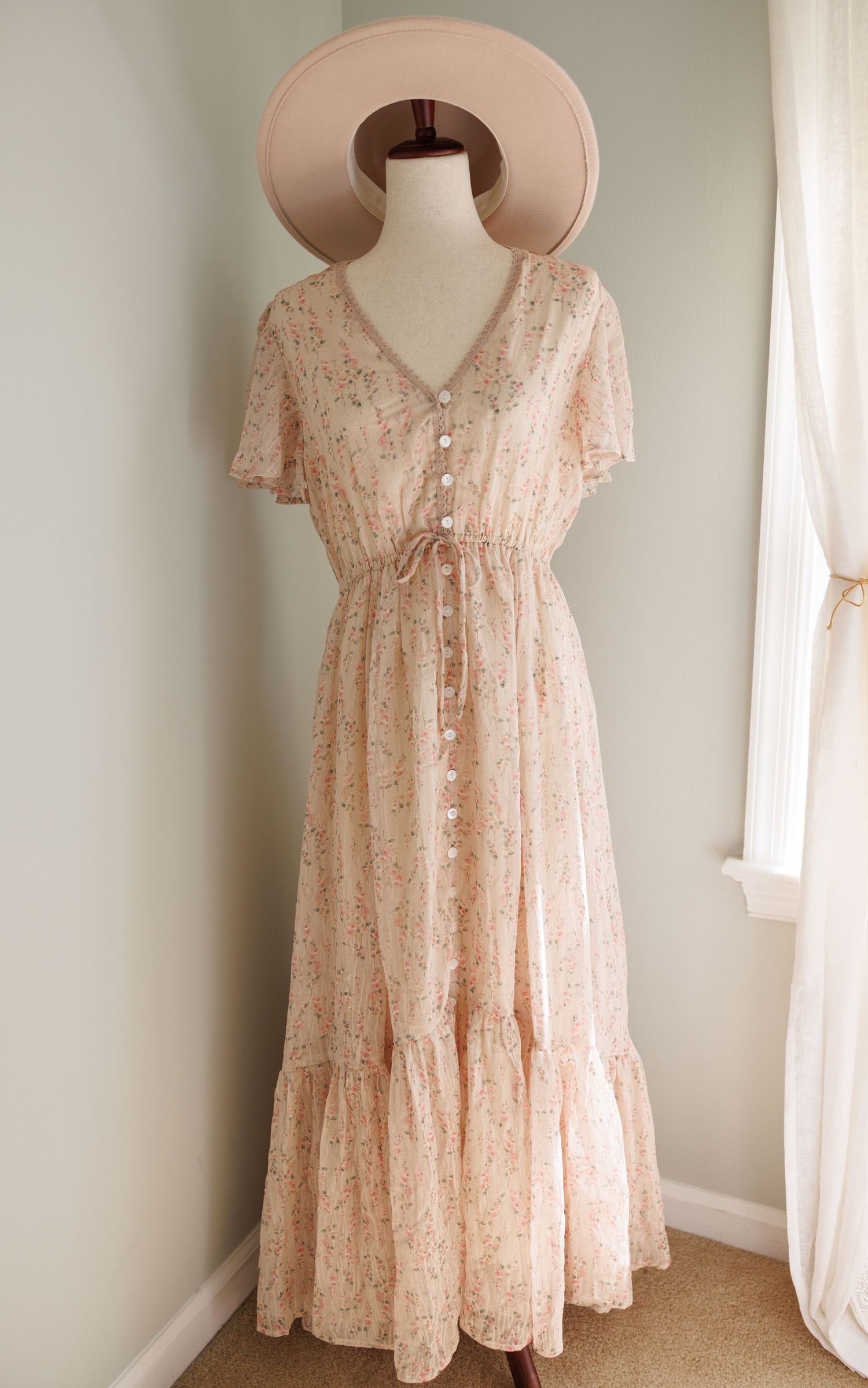 Light pink floral maxi dress with v-neck, short flutter sleeves and tiered ruffle hem displayed on mannequin with matching hat.