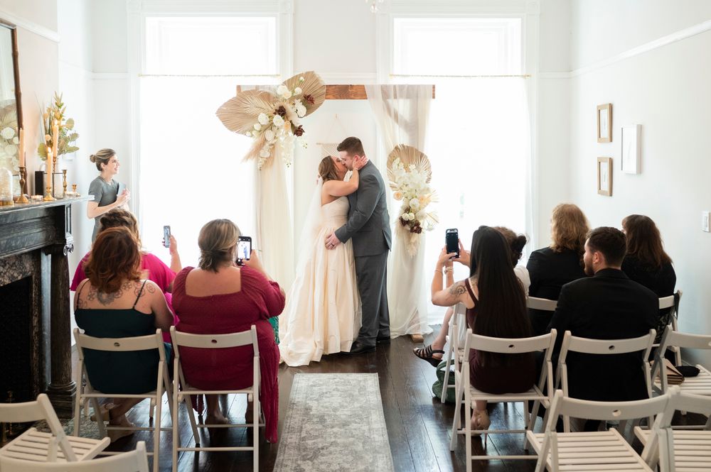 Wedding guests sit in chairs watching a ceremony in a bright, sunlit indoor venue.