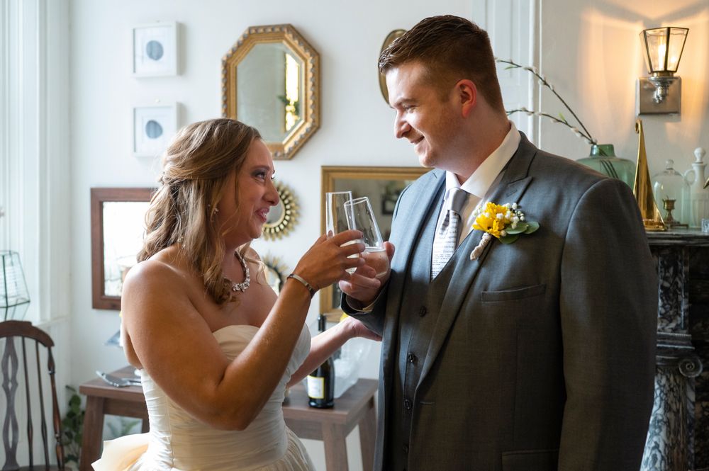 A couple shares a joyful moment during their wedding celebration while holding wine glasses together.
