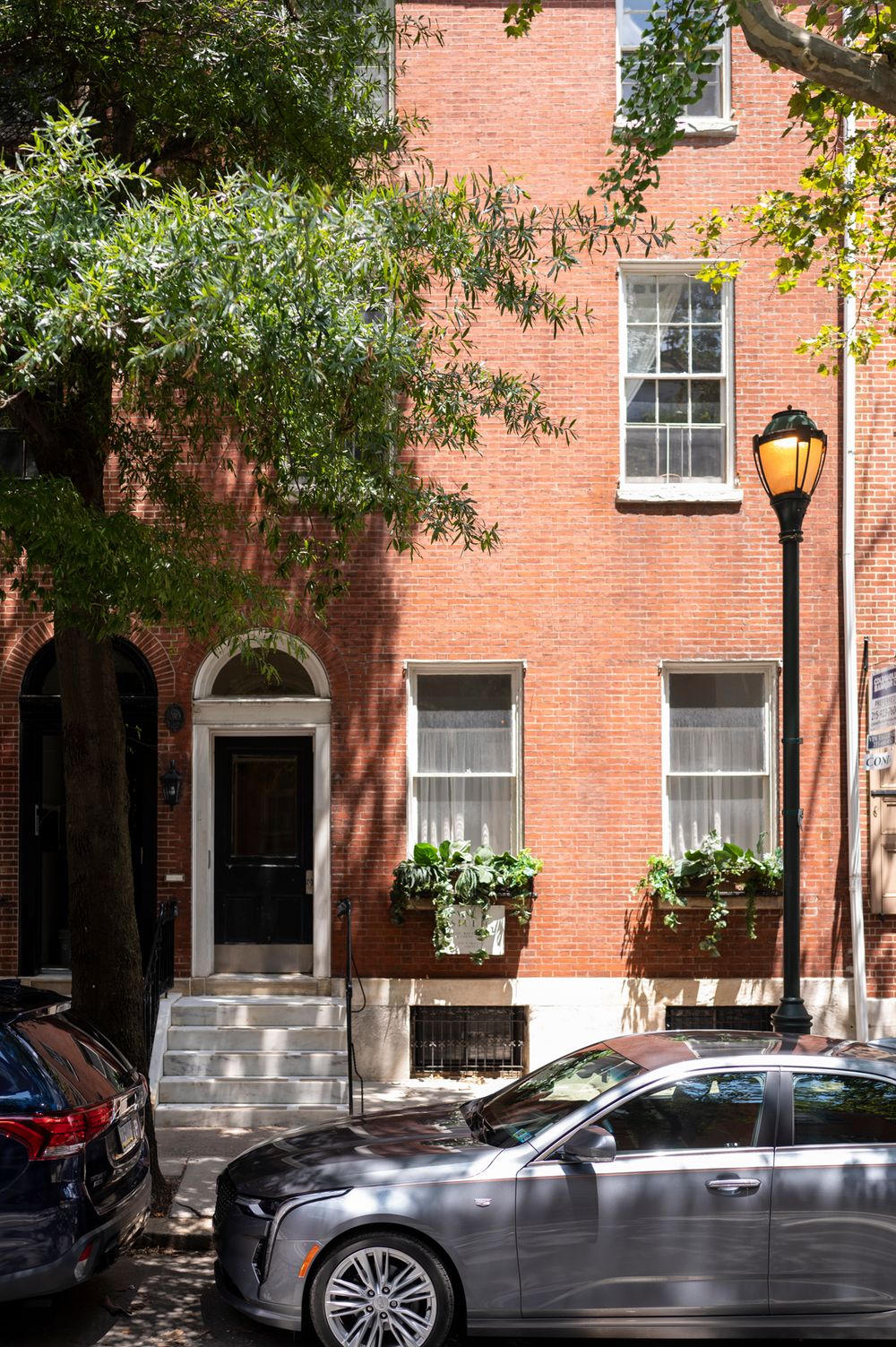 Historic brick townhouses line a tree-shaded street in Philadelphia's Society Hill neighborhood with parked cars along the curb.