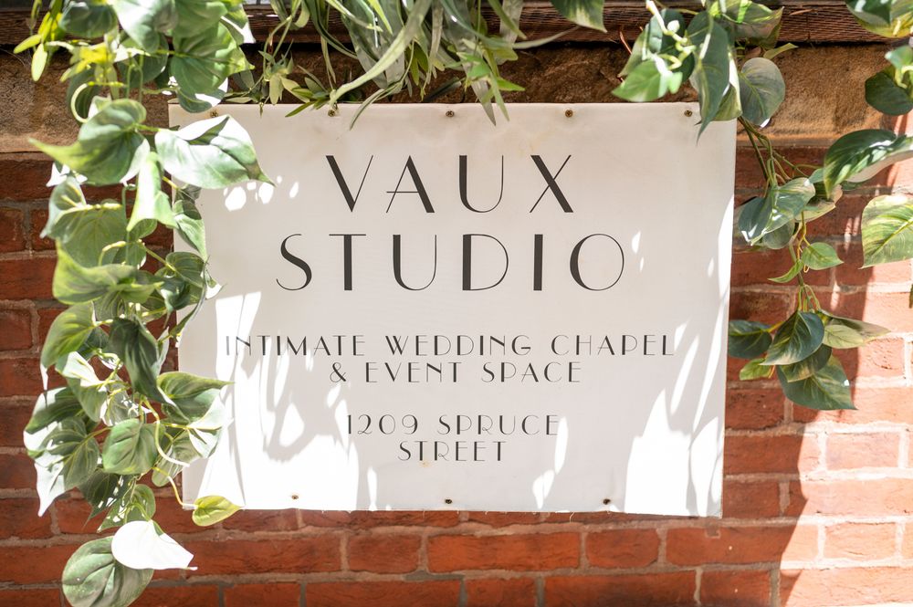 Elegant white studio signage mounted on exposed brick wall with cascading green vines and foliage.