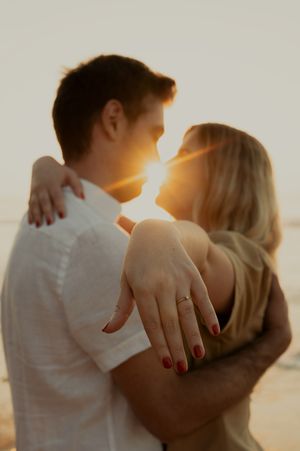 Intimate couple embracing on beach at sunset with ring detail visible.