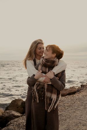 Intimate couple sharing tender moments on a rocky beach at dusk.