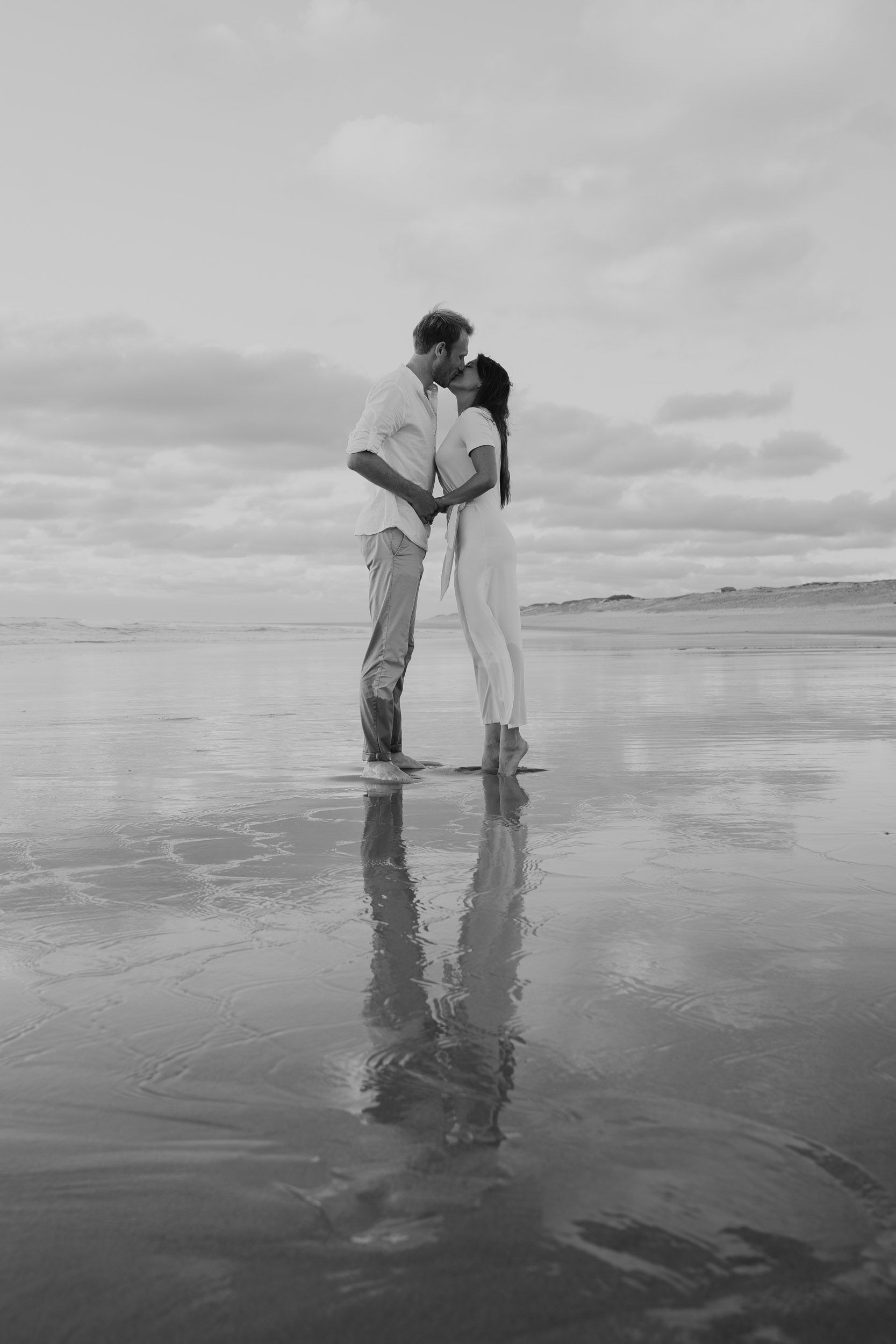 Black and white beach photography showing reflections in wet sand during low tide.