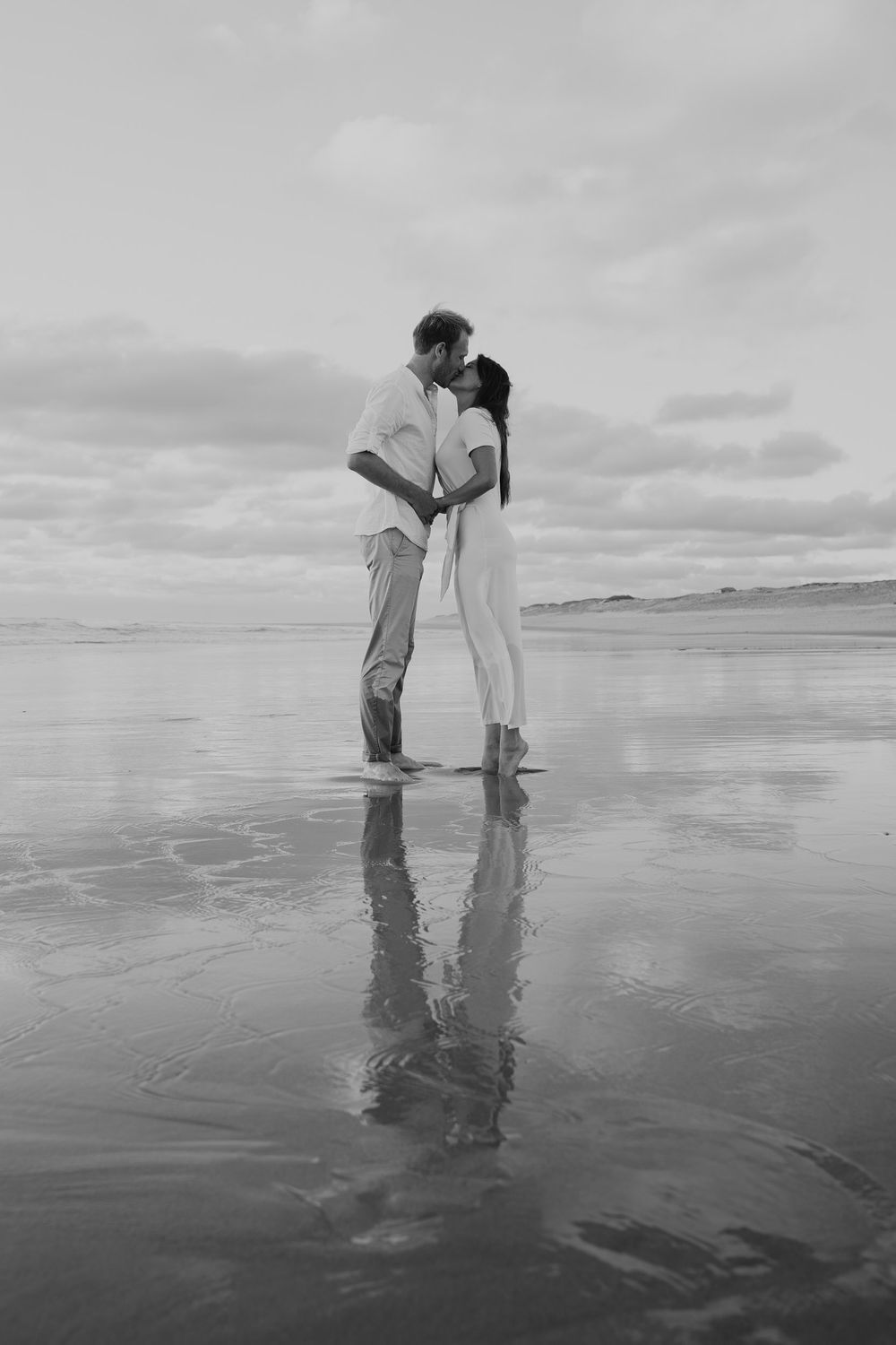 Black and white beach photography showing reflections in wet sand during low tide.