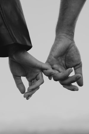Black and white close-up of multiple hands holding each other against light background.