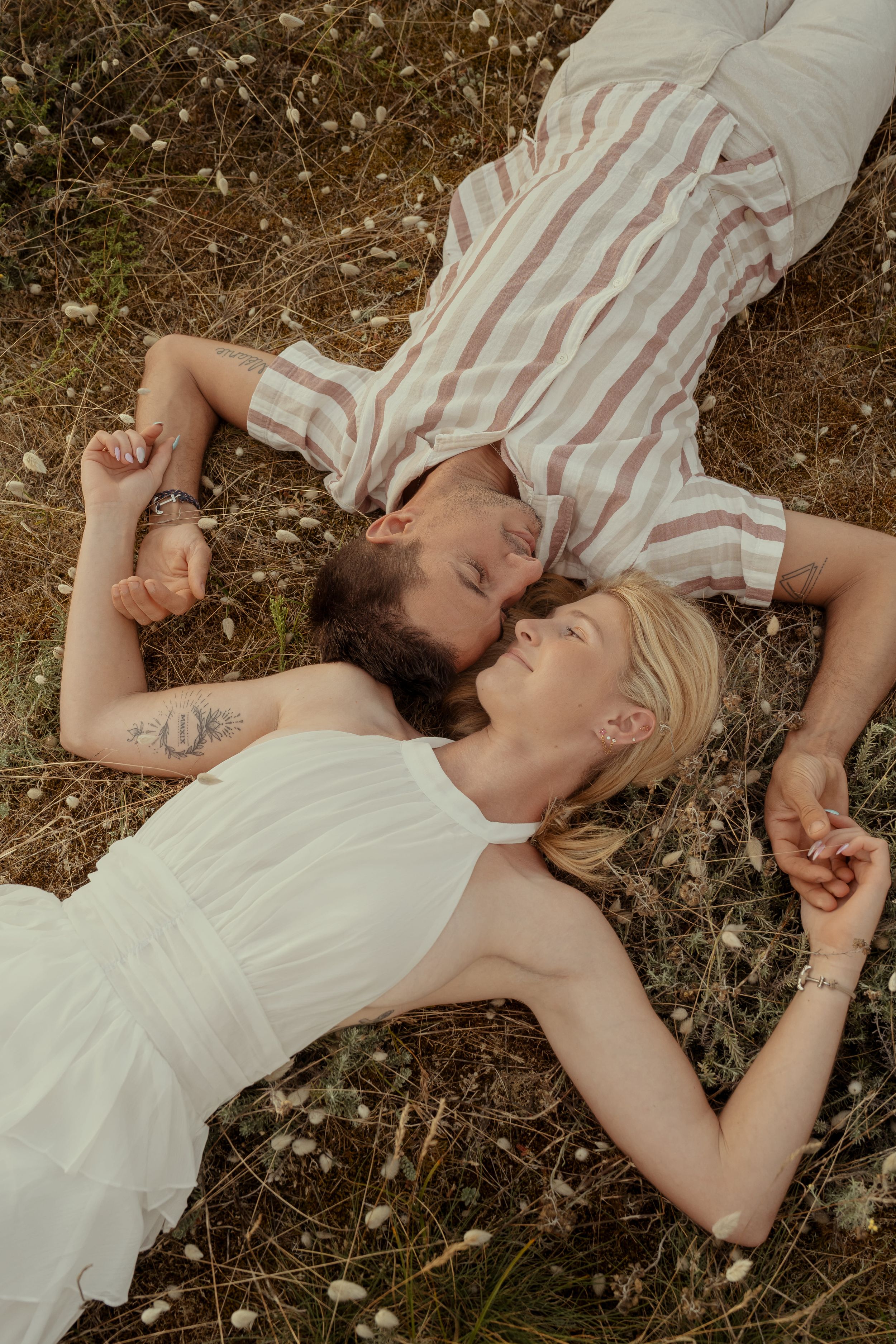 A couple lying in a field of wildflowers wearing white and striped clothing.