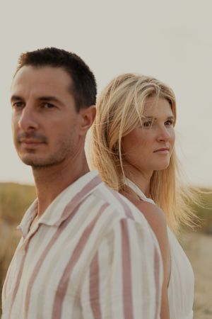 Couple in light colored clothing posing against neutral background during golden hour.