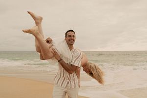 Playful couple in light clothing having fun at the beach during sunset.