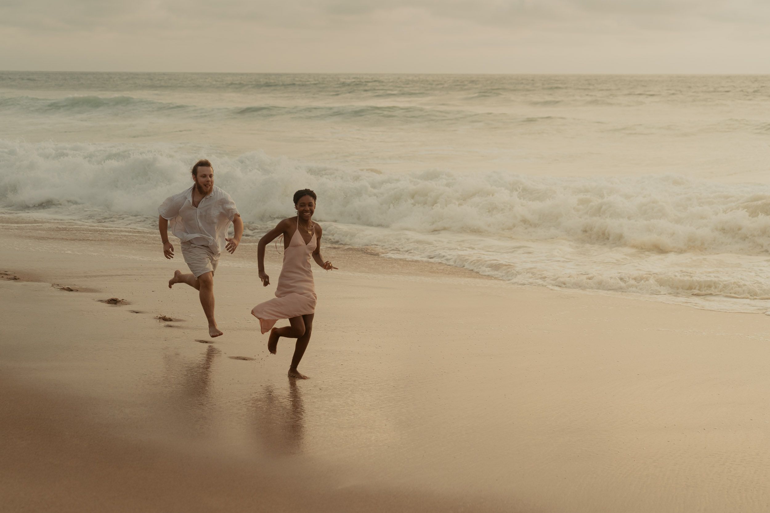 People running and playing on a beach at sunset with golden light.