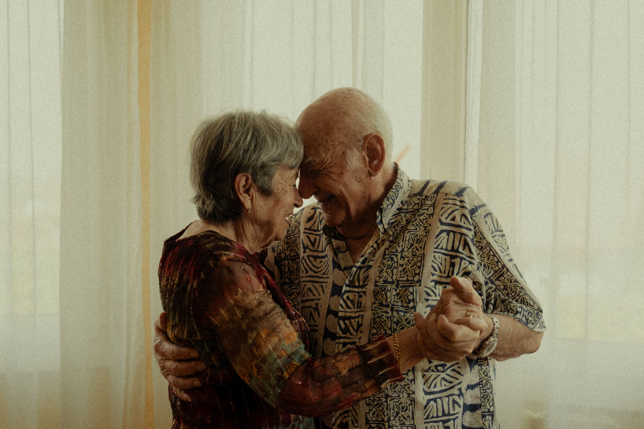 An elderly couple shares an intimate moment together while sitting indoors.
