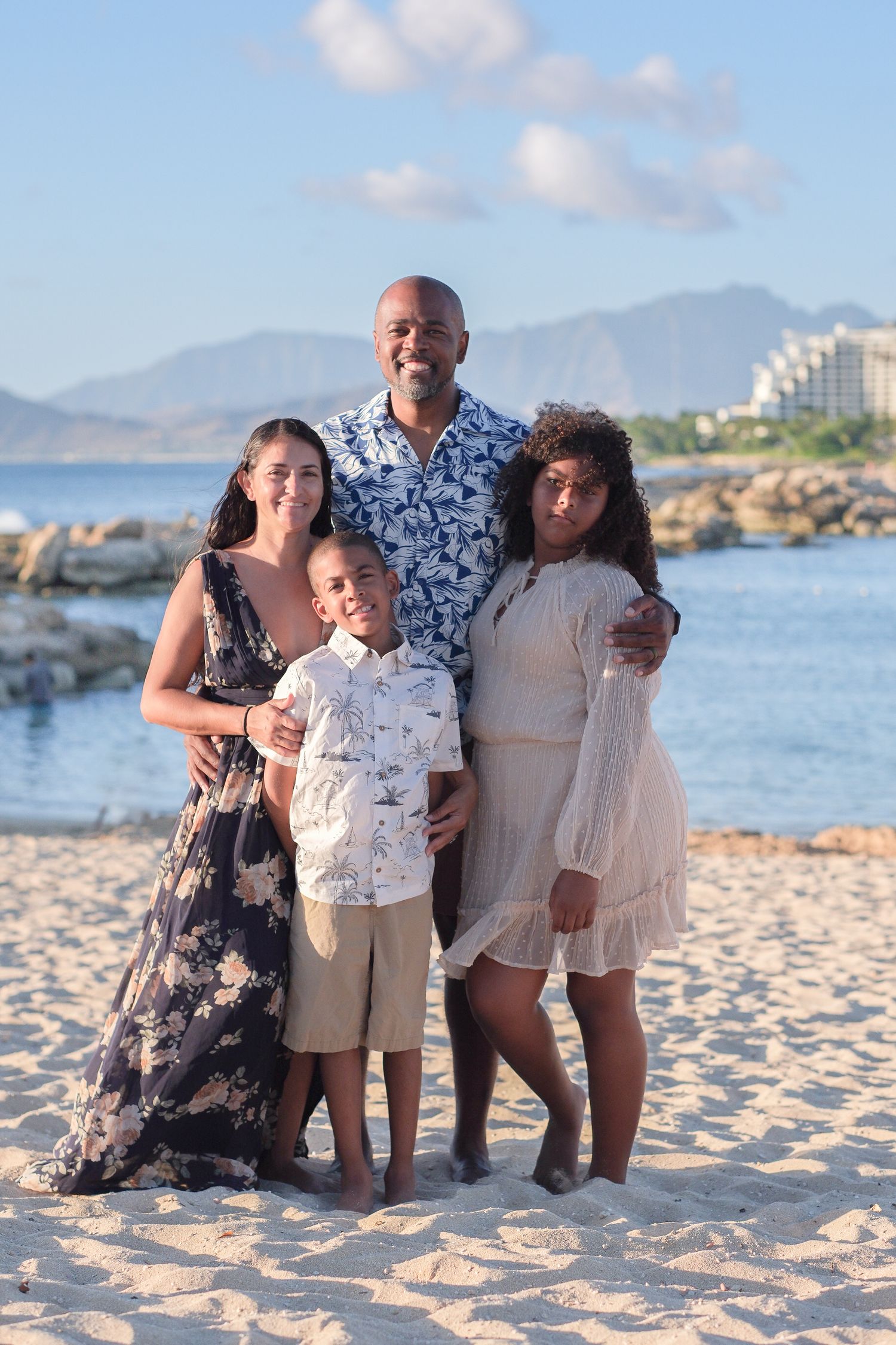 Family portrait session on an Oahu beach featuring ocean views and coastal mountain scenery.