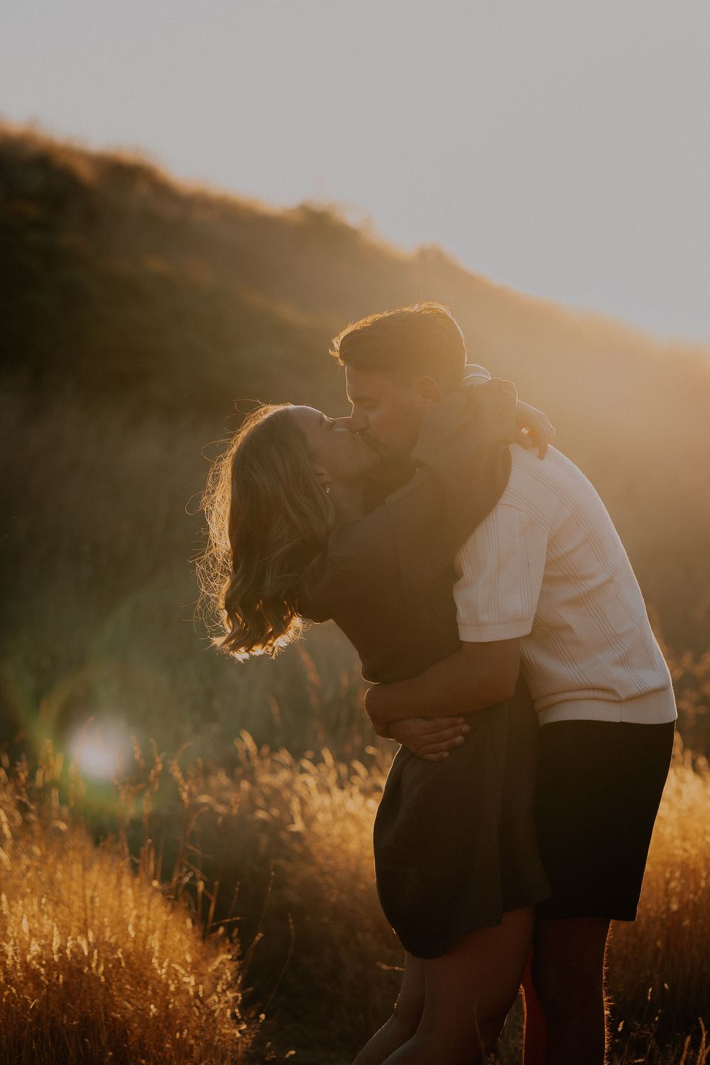 A romantic couple shares an intimate moment in a sunlit field during golden hour.