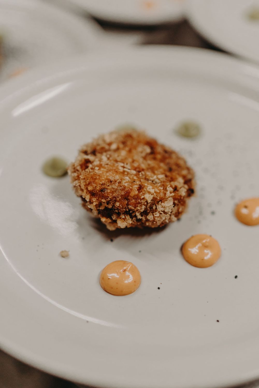 Crispy breaded cutlet served on a white plate with two dots of creamy orange sauce.