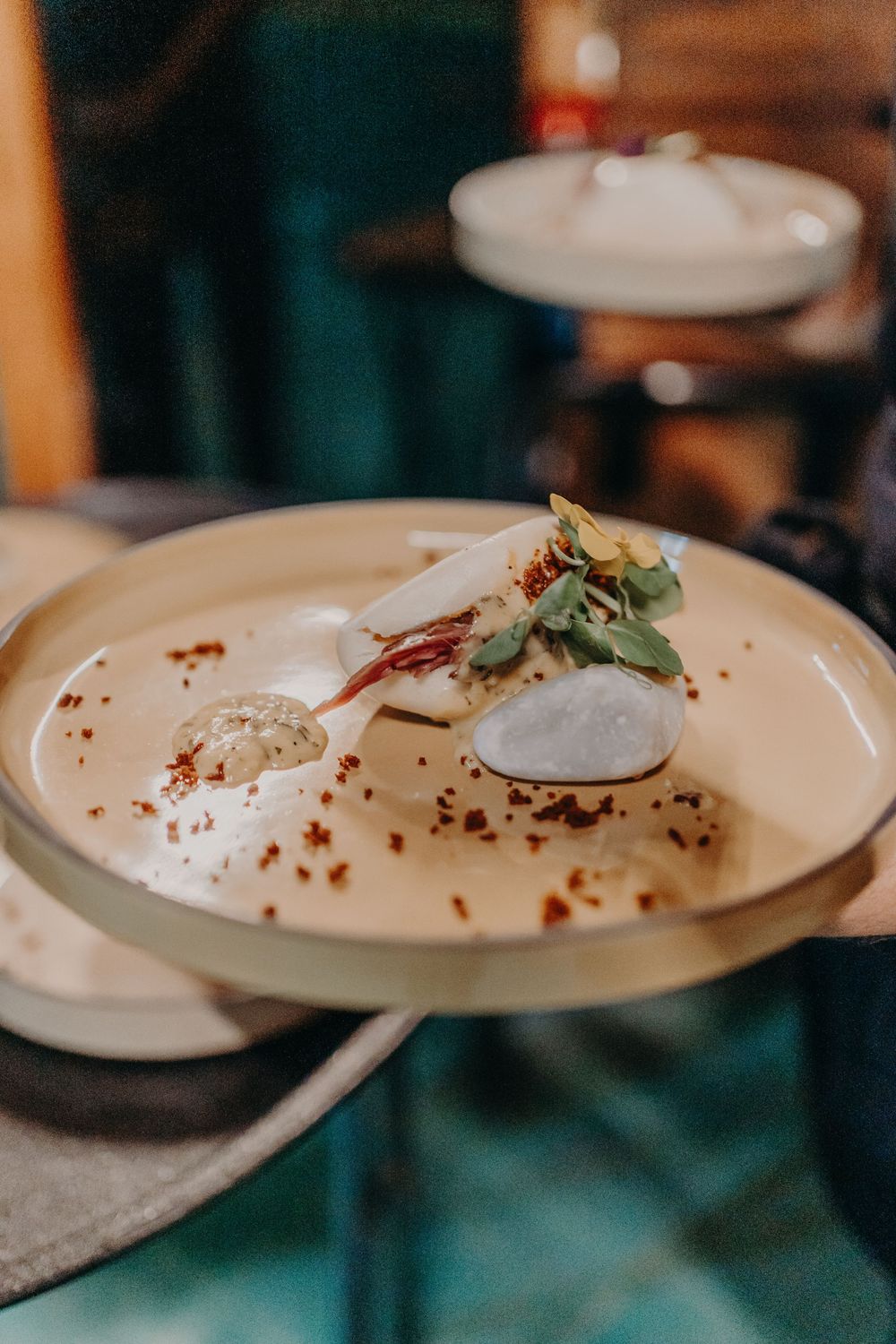 Elegant plated dessert with meringue, microgreens and spice garnish on white ceramic dish in upscale restaurant setting.