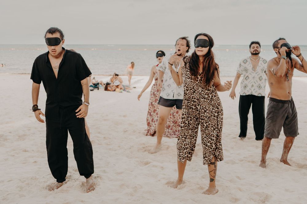 People holding hands and dancing together in a line on a sandy beach during sunset.