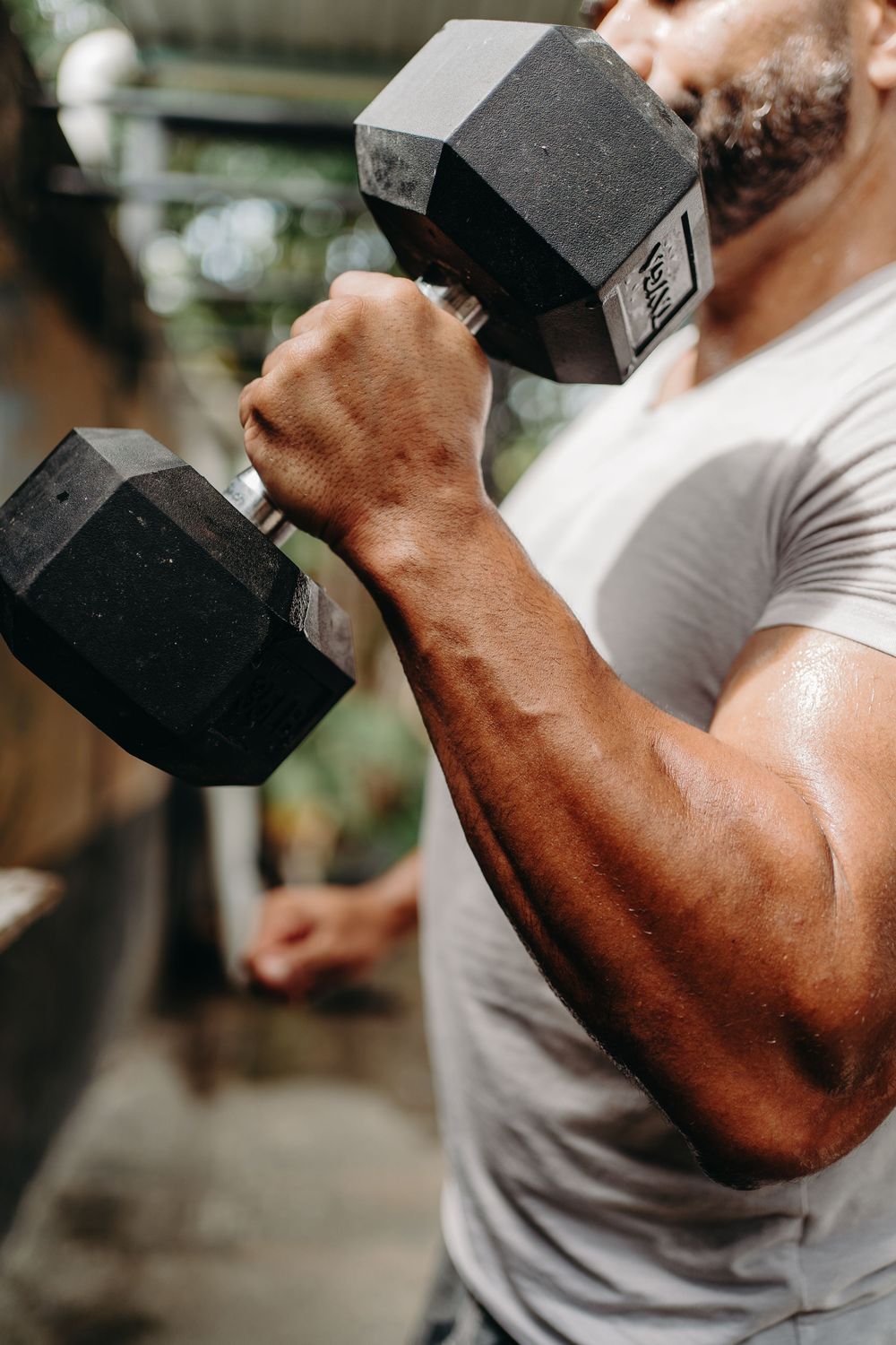 Close-up sequence showing muscular arm curling a heavy black dumbbell during strength training workout.