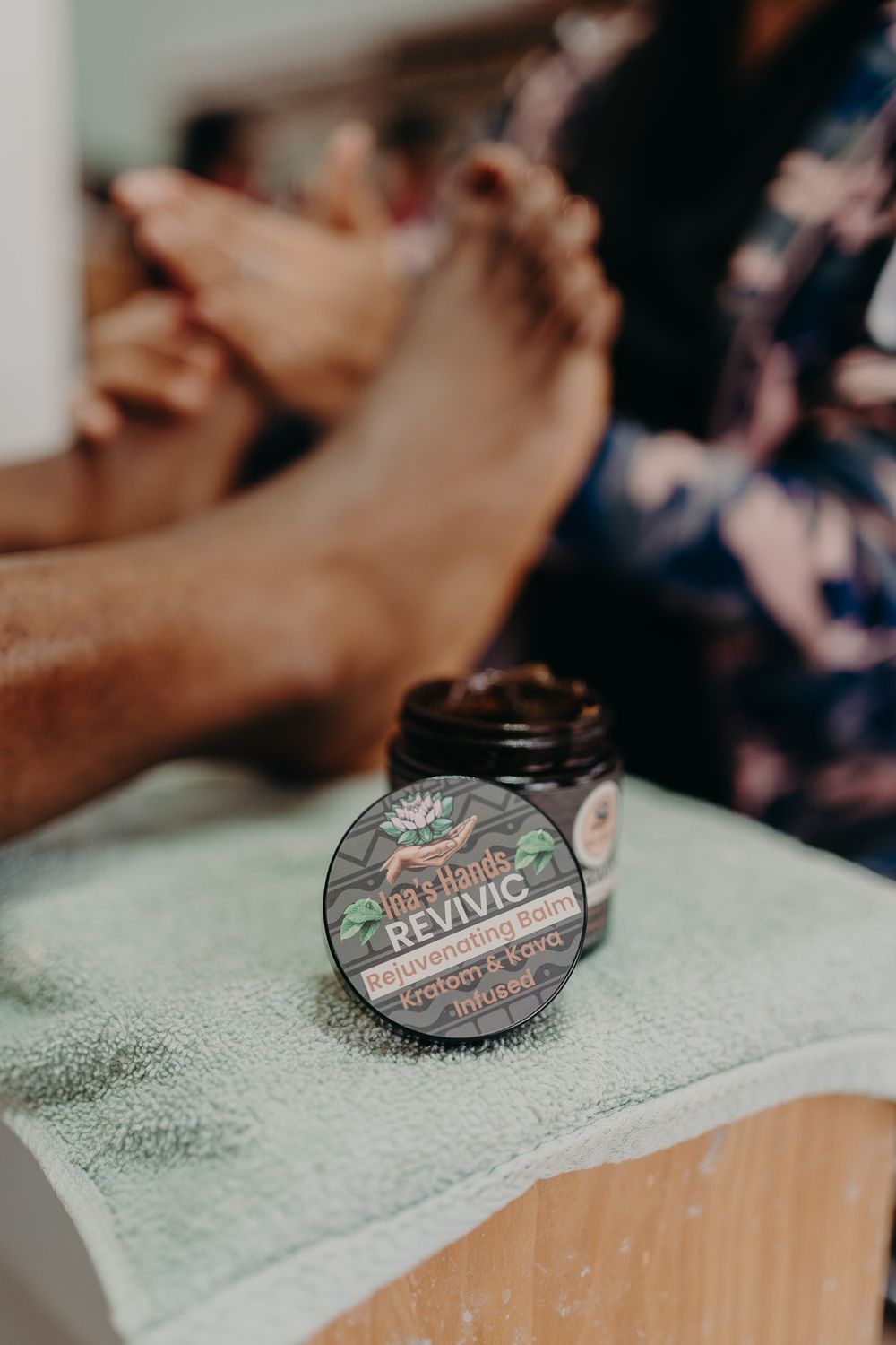A jar of Revival beard balm sits on a white towel with blurred hands in the background.