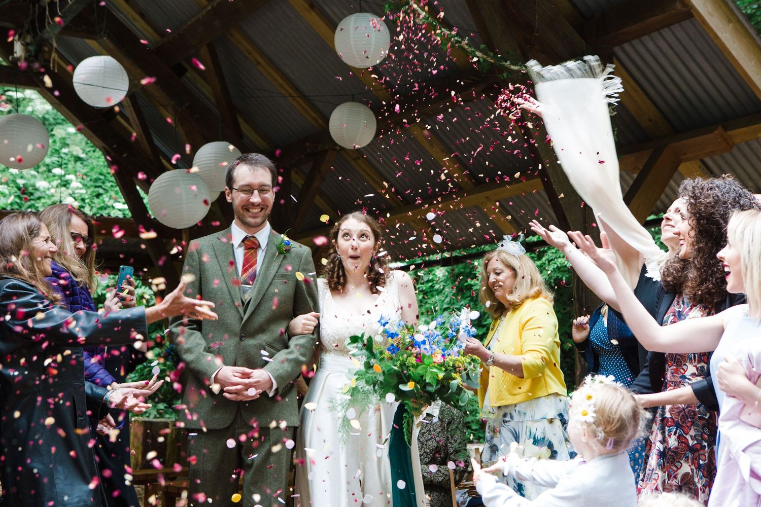 Wedding guests celebrate by tossing colorful confetti in the air during an outdoor celebration.