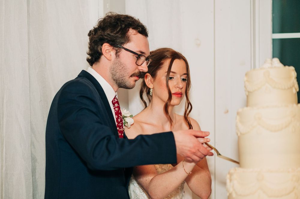 A couple shares a sweet moment while cutting their elegant white wedding cake at their reception.