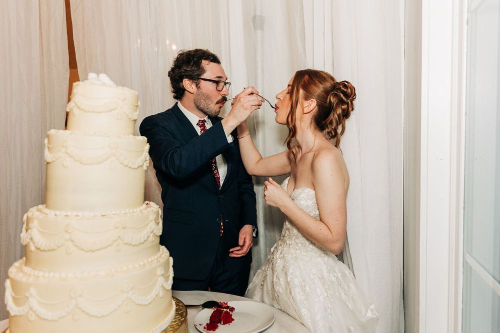 A happy couple shares a romantic moment while cutting their elegant white wedding cake at their reception.