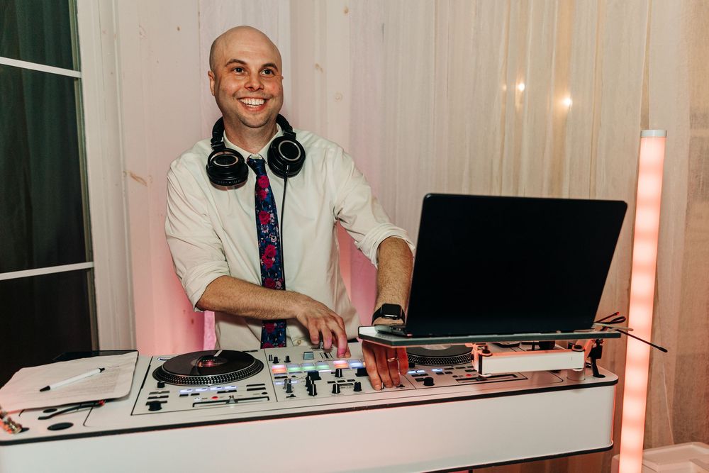 A DJ performs at a mixing console with headphones and equipment in a dimly lit setting.