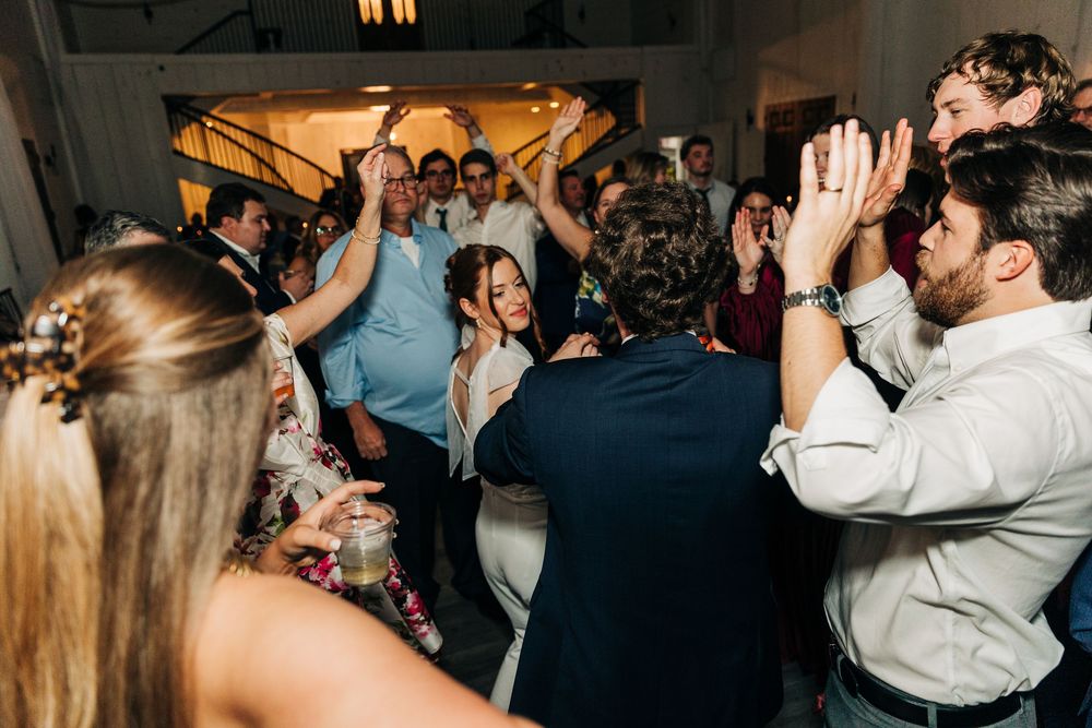 A lively crowd of wedding guests dancing and socializing at an indoor reception venue.