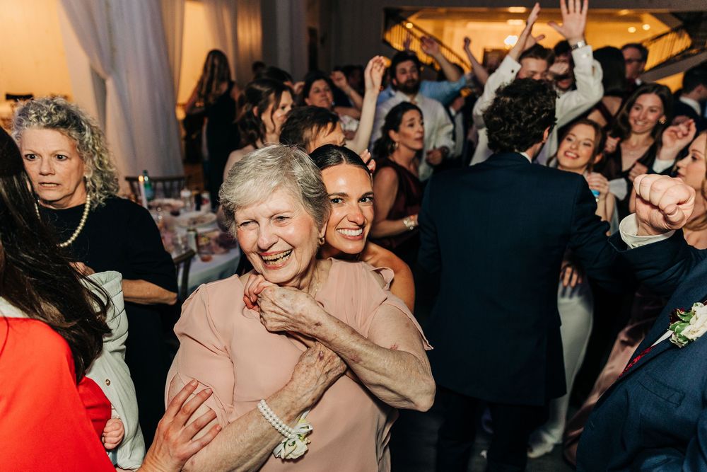 Wedding guests dance and celebrate together on a crowded dance floor under warm lighting.