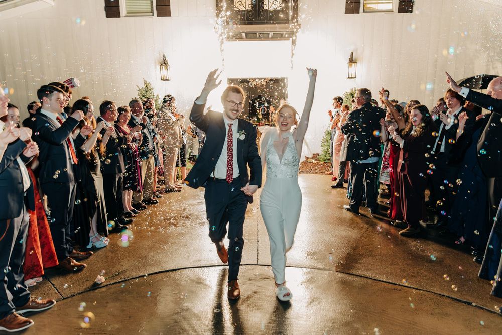 Wedding guests line both sides of a bright indoor venue as they watch a couple's first dance on the dance floor.