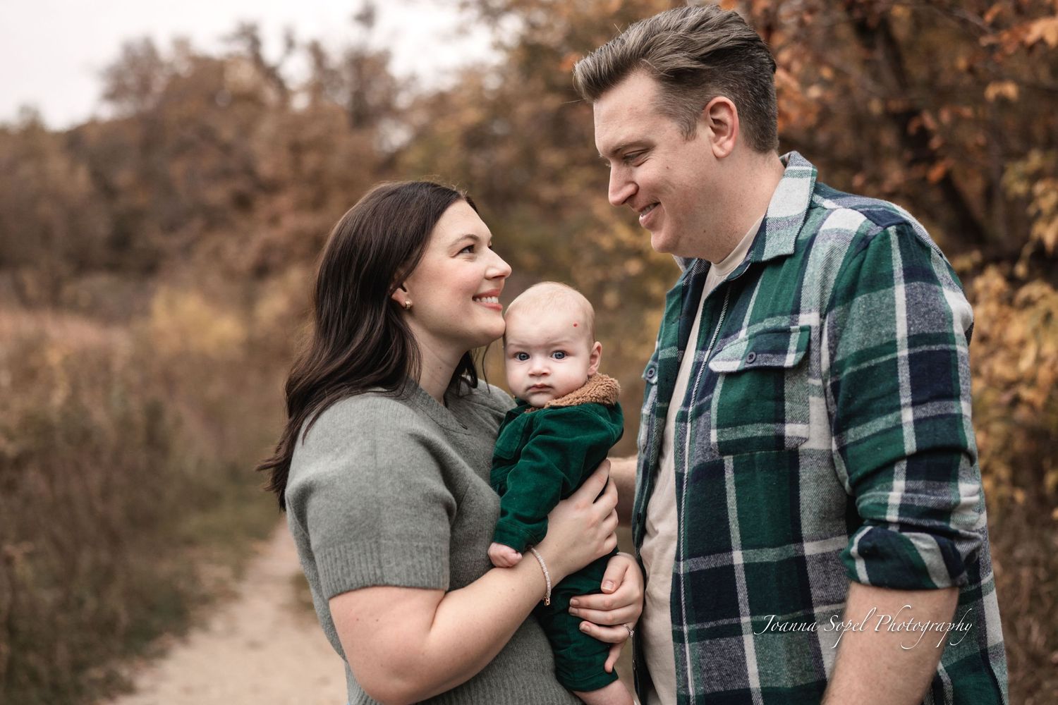 A family enjoying a tender moment together outdoors during autumn with warm earth tones and fall foliage in the background.