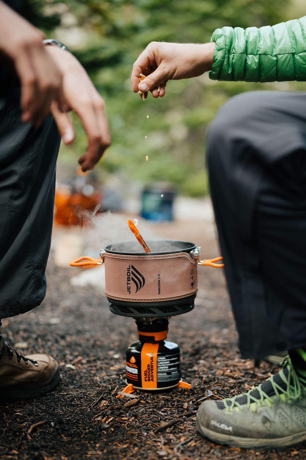 Adding ingredients to a Jetboil camping stove while cooking outdoors.