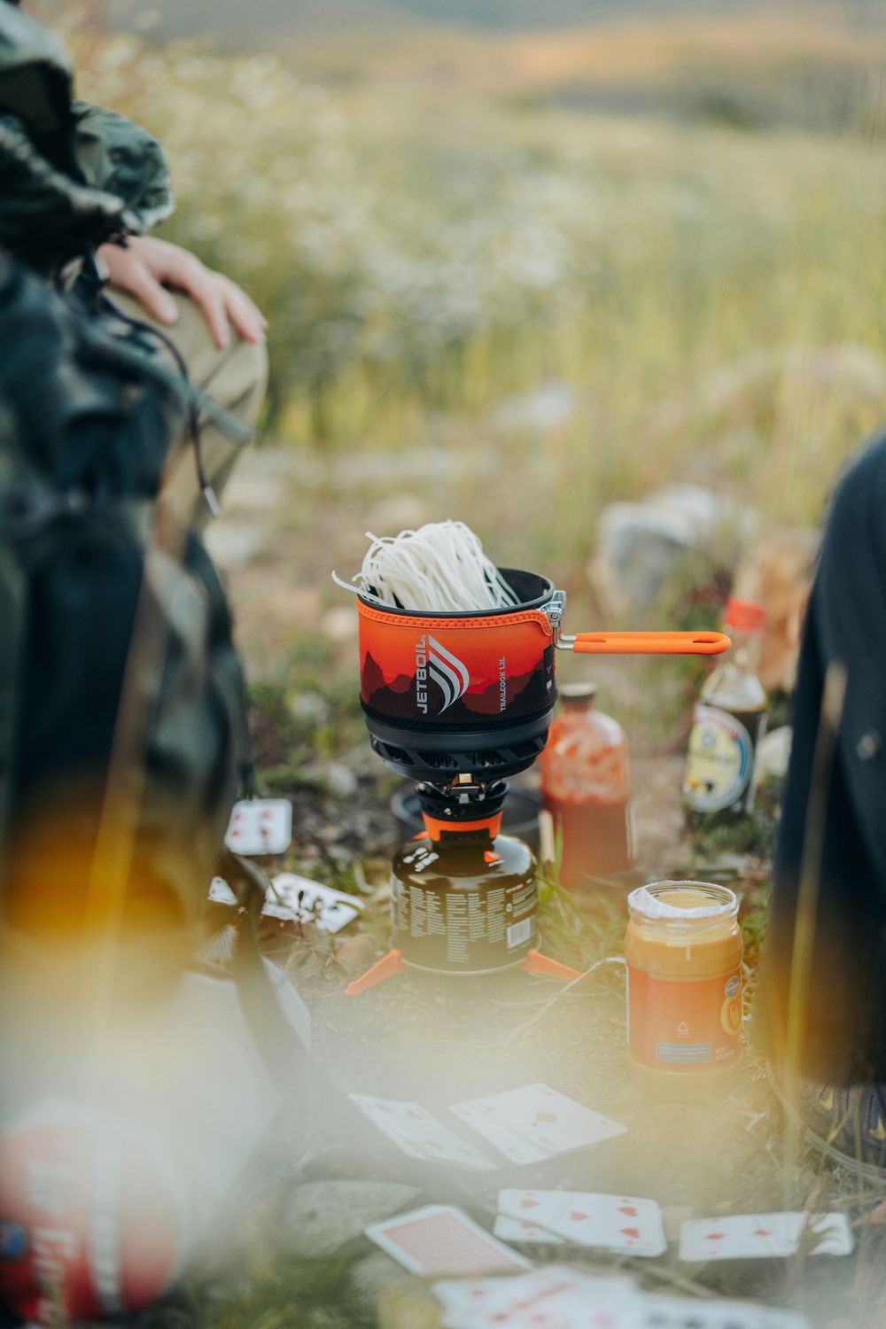 Camping cookware and supplies arranged on a rustic outdoor table during sunset with a blurred foreground.