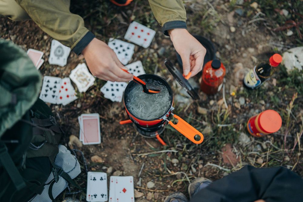 Playing cards and camping gear scattered on forest ground during an outdoor adventure.