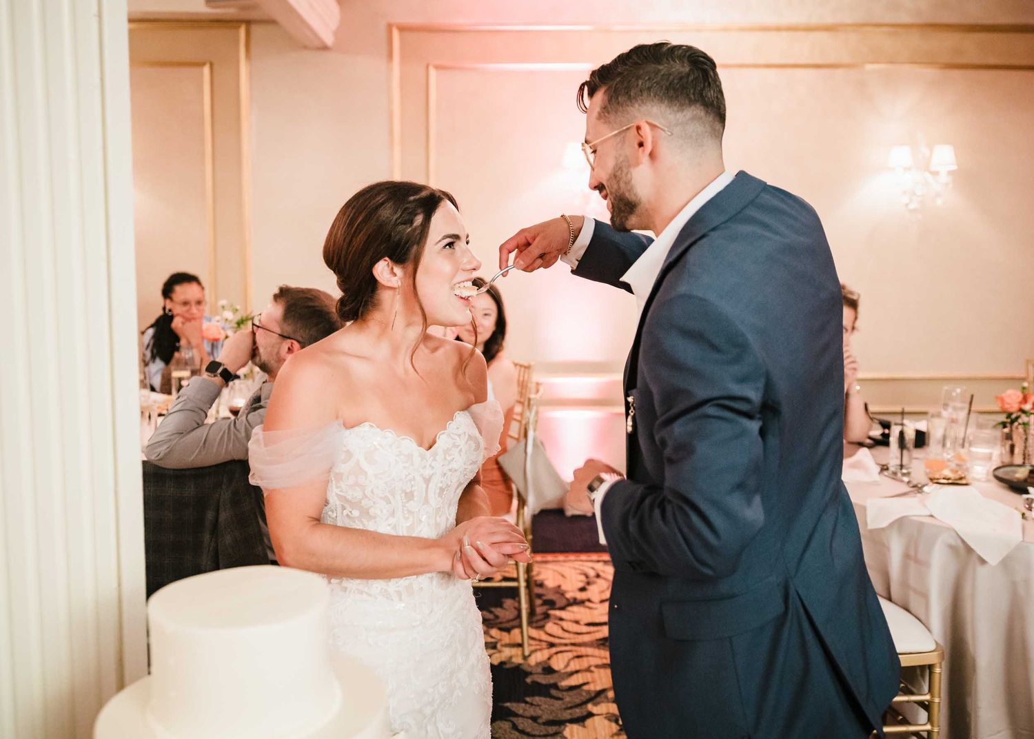 Groom feeds cake to bride as guests watch during a wedding reception at the Lenox Hotel in Boston