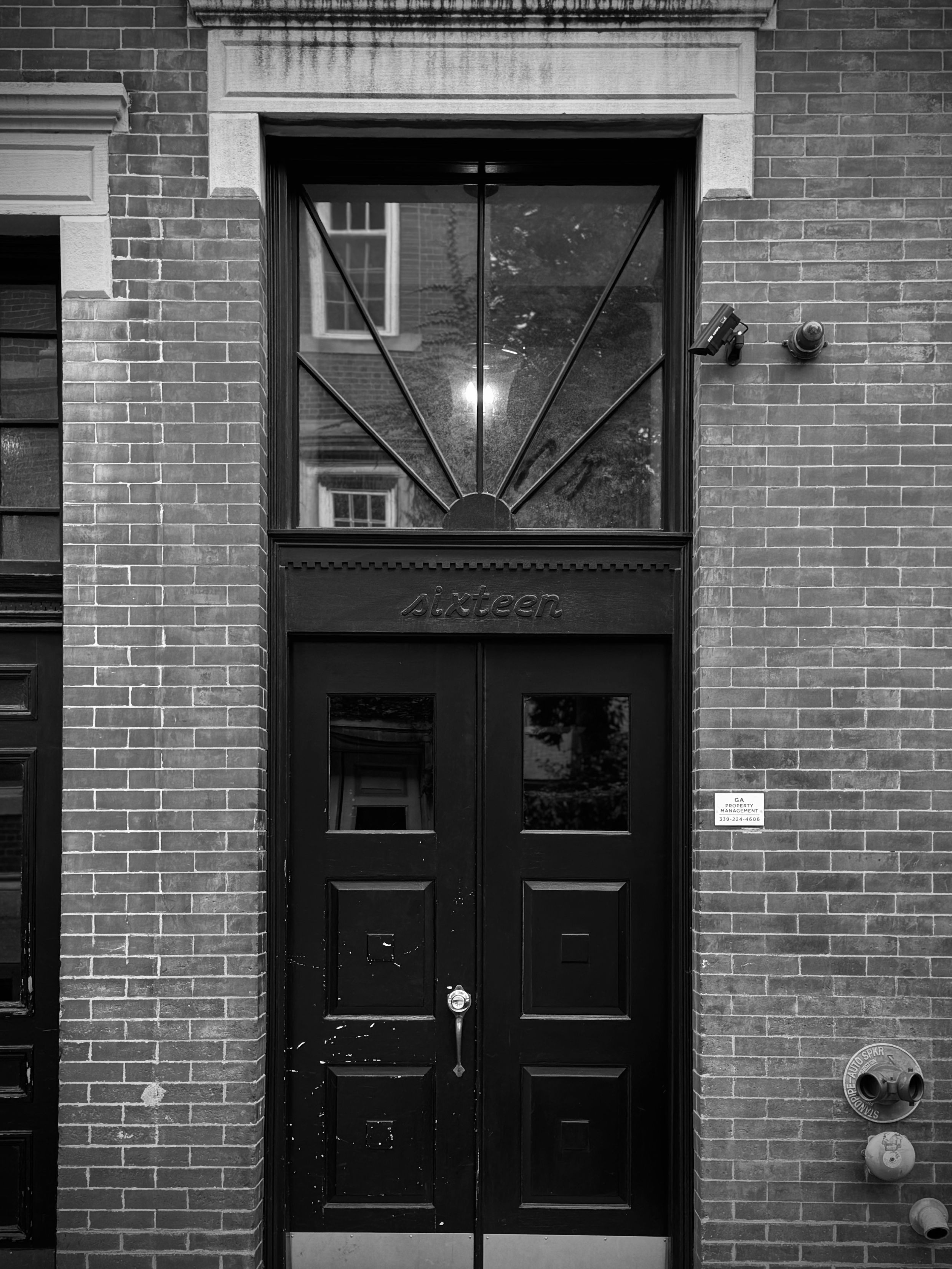 Art deco style black double doors with geometric transom window set in red brick facade of historic building.