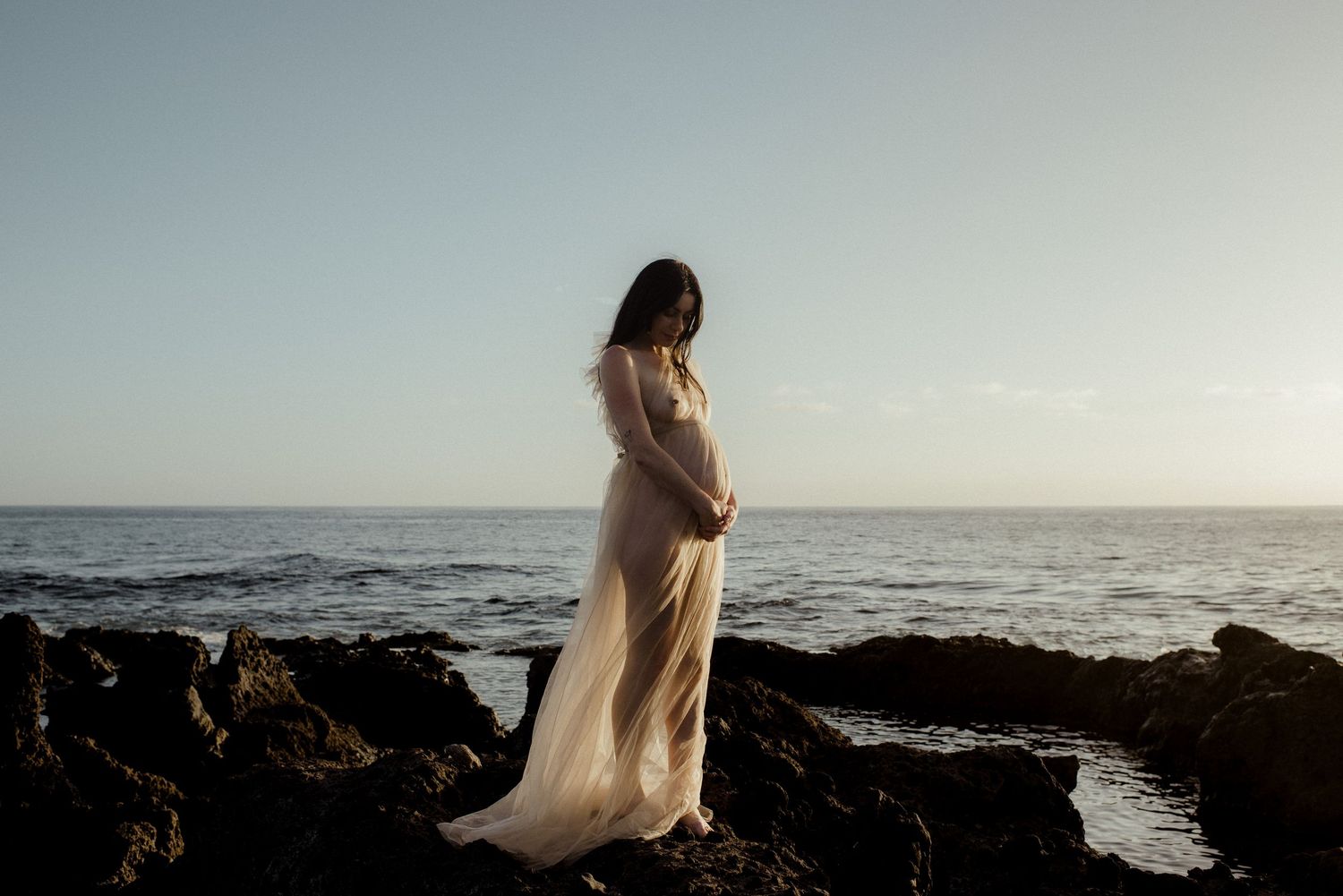 A silhouetted figure stands on a rocky cliff edge overlooking a misty ocean landscape at dusk.