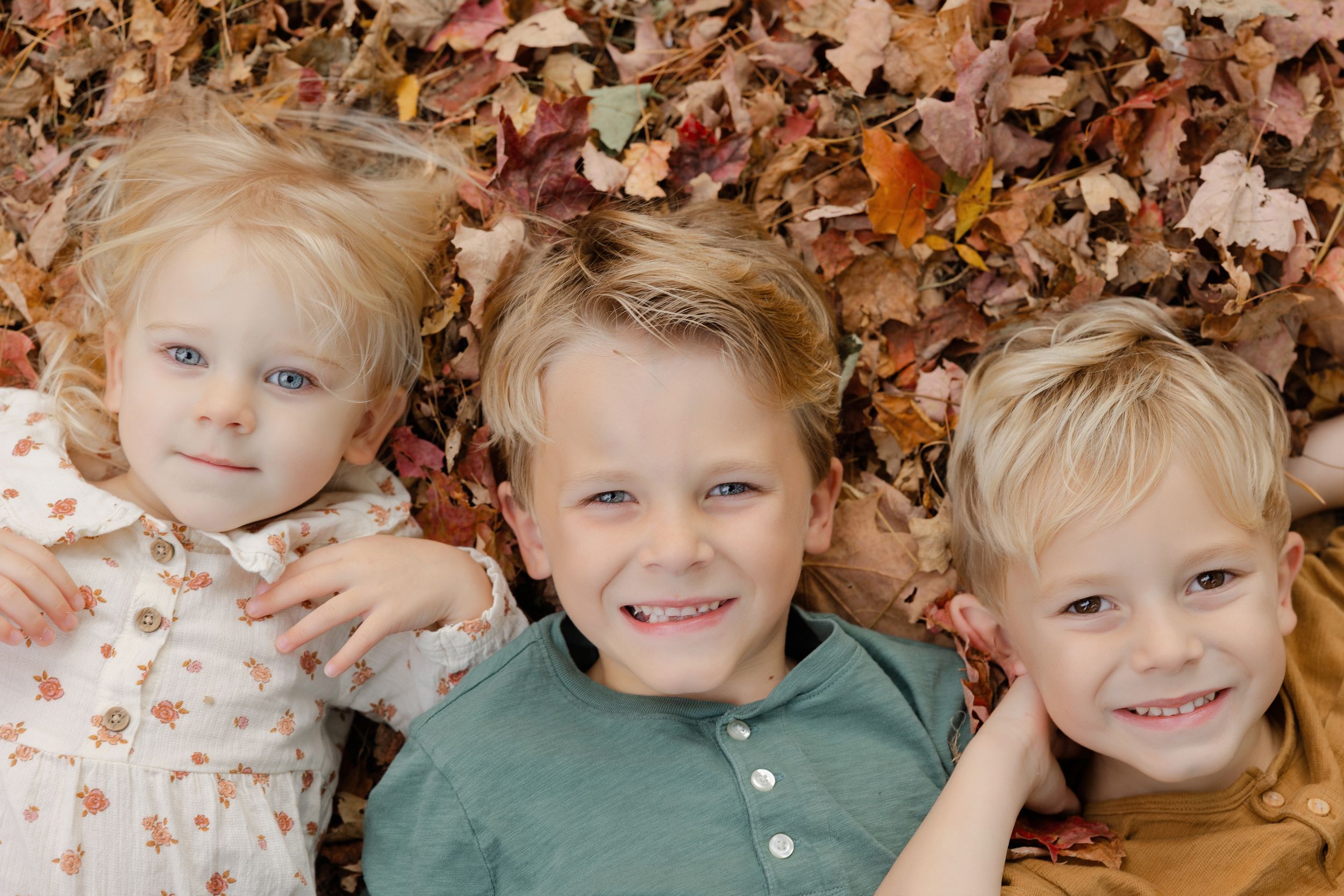 Children lying in a circle formation on autumn leaves wearing green and white clothing.