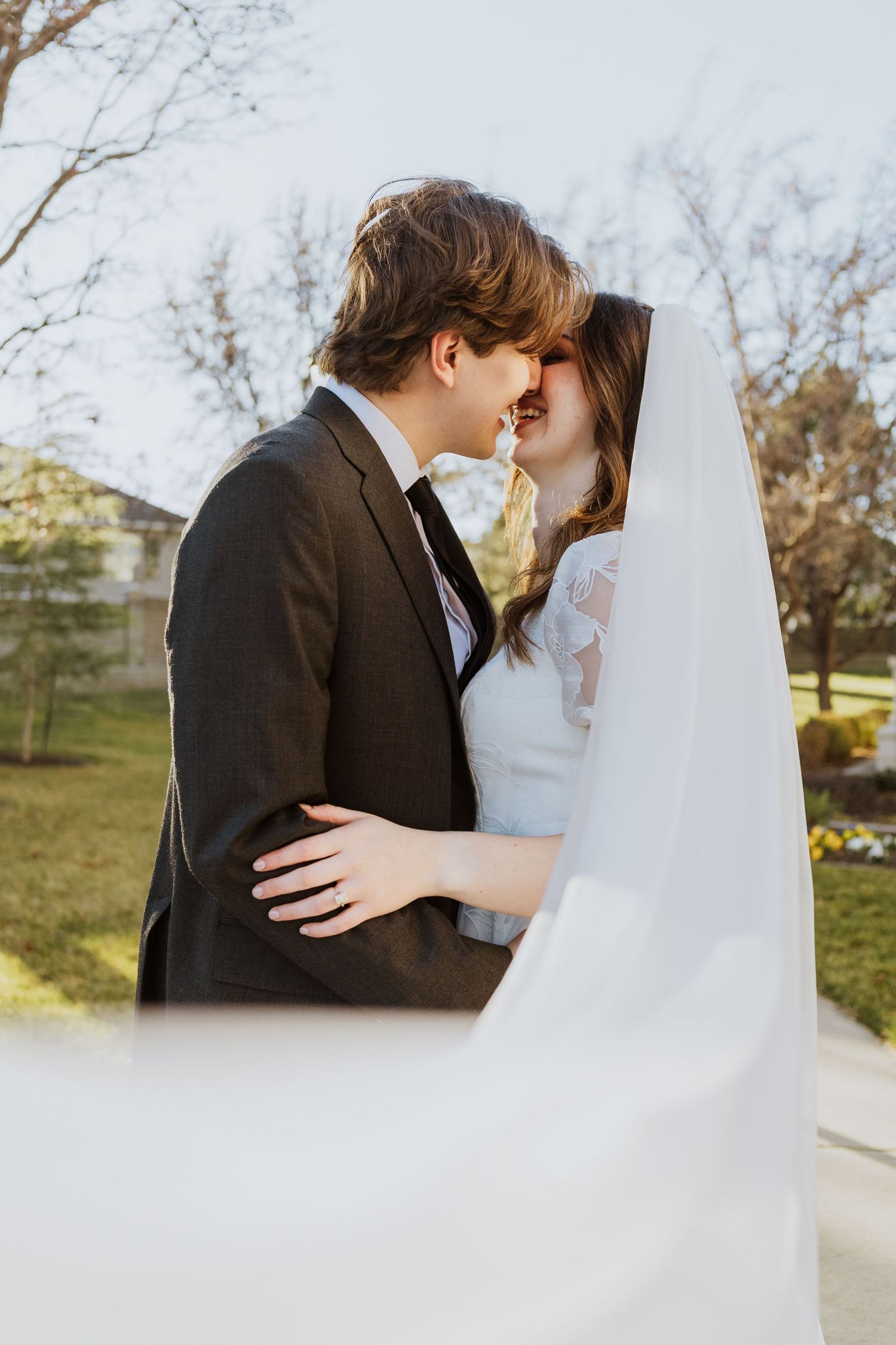 The bride and groom lean in for a kiss while her veil is pulled close to the camera