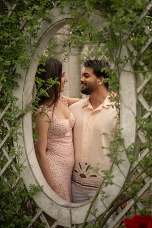 Smiling couple gazing at each other framed by a circular white trellis covered in green vines.